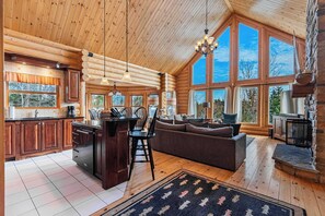 Ein Holzblockhaus-Interieur mit Küche, Essbereich und Wohnzimmer, mit großen Fenstern und Holzbalkendecken.