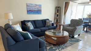 Un salon avec un canapé, un fauteuil, une table basse et un tableau accroché au mur.