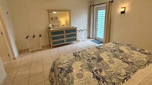 Une chambre à coucher comprenant un lit, une commode, un ventilateur de plafond, une fenêtre avec des rideaux et une porte.
