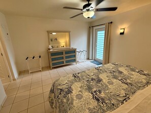 Ein Schlafzimmer mit Bett, Kommode, Deckenventilator, Fenster mit Vorhängen und einer Tür.