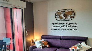 Un saló amb un sofà morat, dos petjacs blancs, una taula de centre de fusta i un rellotge de paret decoratiu.
