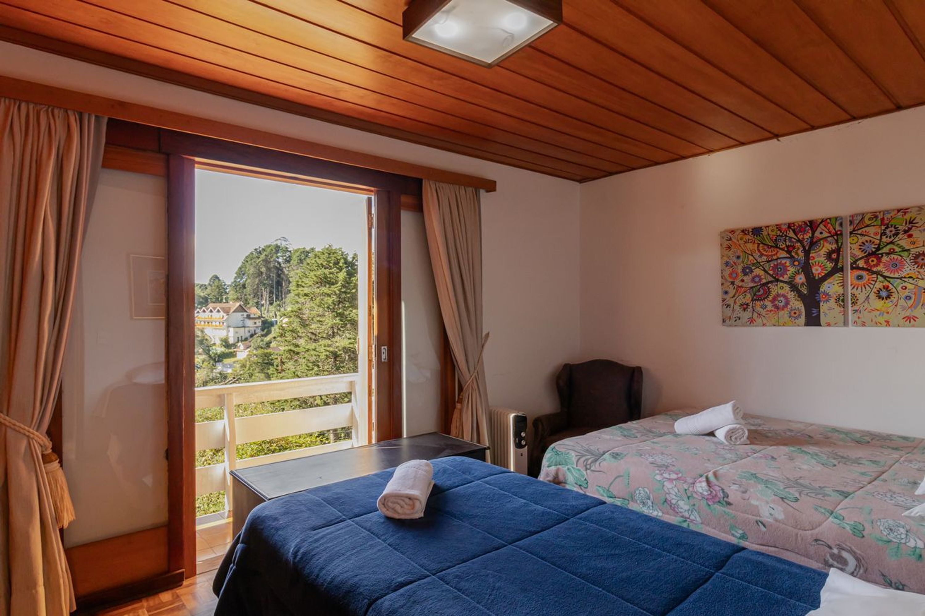 A room with two beds, a view through a sliding door, a painting on the wall, and a ceiling light.