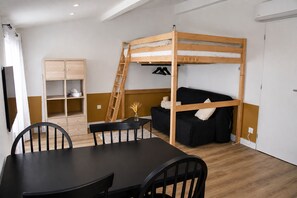 Una cama tipo litera con escalera, un sofá negro, un armario de madera y una mesa de comedor con sillas.