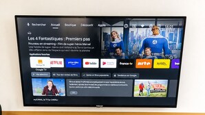 Un téléviseur fixé au mur, avec une étagère en bois en dessous.