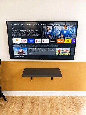 A television mounted on a wall with a wooden shelf below it.