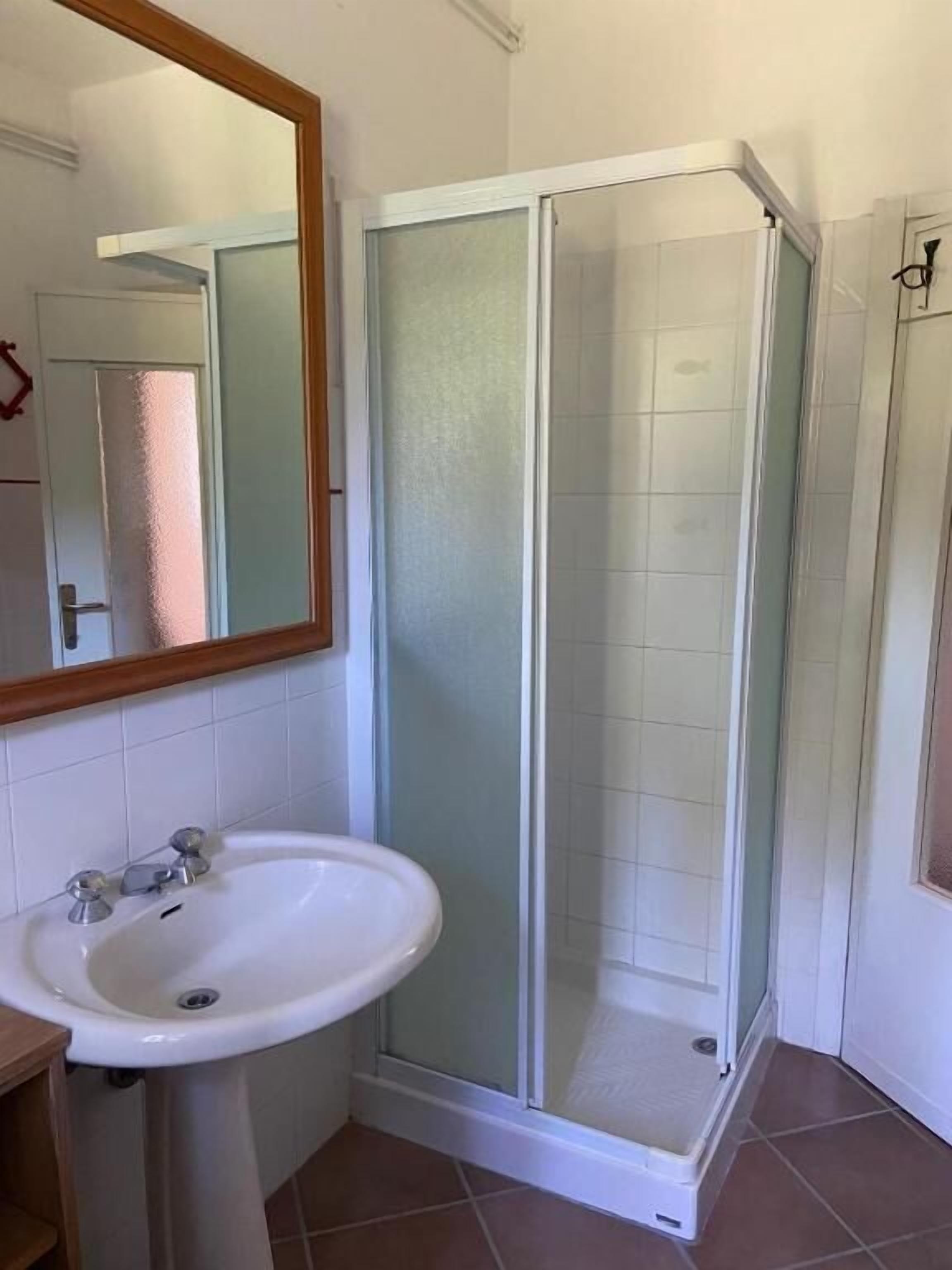 A bathroom with a glass-enclosed shower, a white sink, and a mirror.