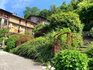 A residential area with a red metal gate, lush greenery, and a staircase leading uphill. - Natura tra bosco e lago (Castelveccana)