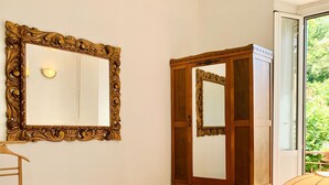 Une chambre à coucher avec un lit, une armoire en bois, un miroir et une fenêtre donnant sur un paysage verdoyant.