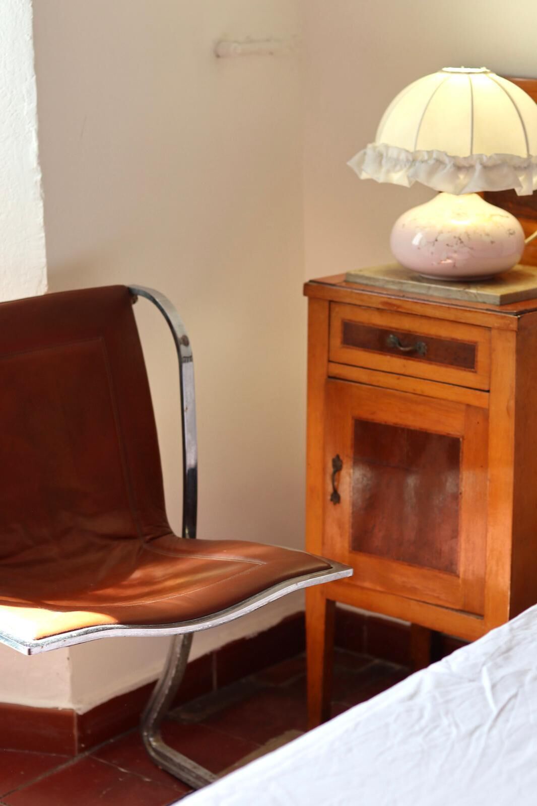 Une chaise avec un cadre en métal, un meuble en bois avec un tiroir et une lampe posée sur le dessus.