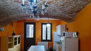 Une pièce avec un plafond en briques, une table à manger, un coin cuisine équipé d’un réfrigérateur et une fenêtre avec des volets.