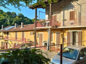 A two-story building with a balcony, a car parked in front, and a view of a hillside. - Natura tra bosco e lago (Castelveccana)