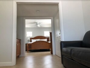Un pasillo que conduce a un dormitorio con una cama, un ventilador de techo y una puerta.