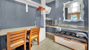 Un angolo cottura compatto con forno a microonde, un lavandino piccolo e una sedia di legno.