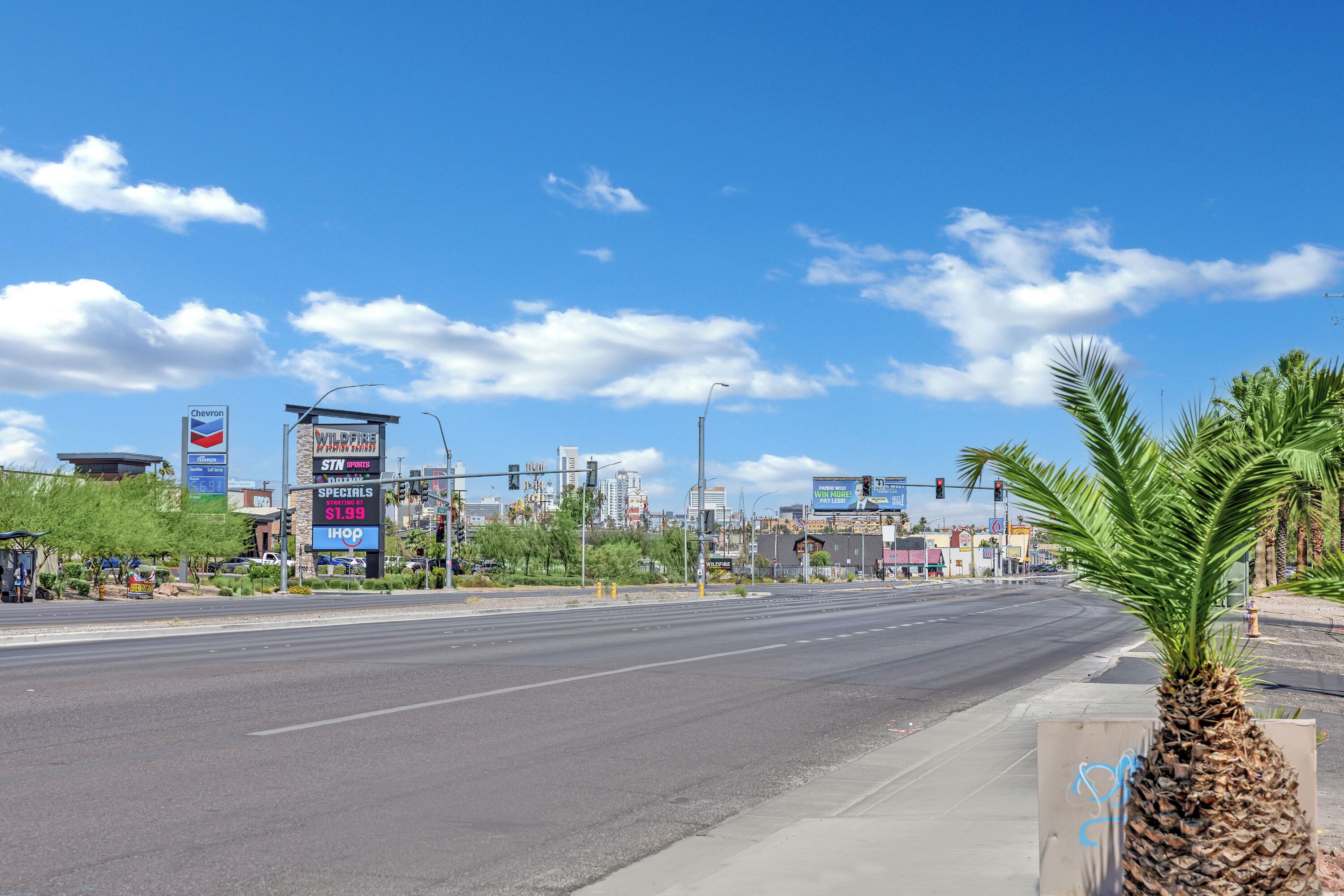 A wide street with palm trees, a Chevron sign, and a 5-star hotel in the background.