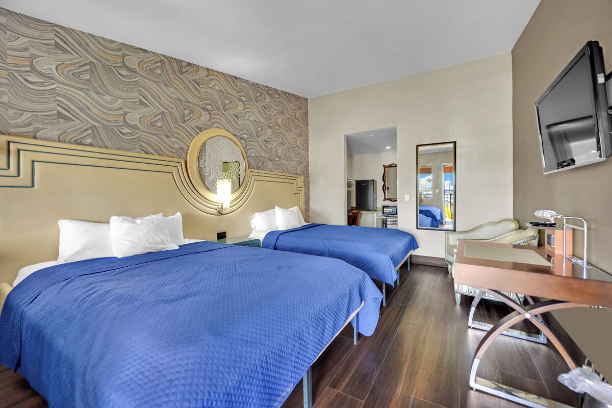 Habitación de hotel con dos camas, un escritorio, un espejo y un televisor.
