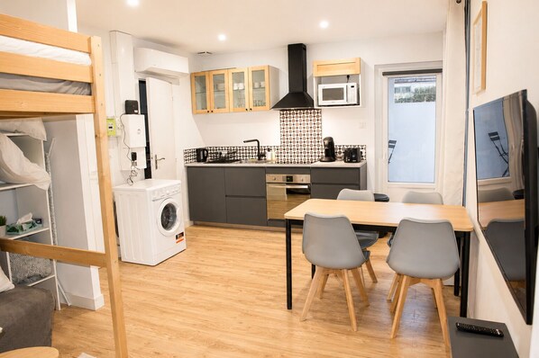 Un espacio habitable compacto con kitchenette, comedor y lavadora.
