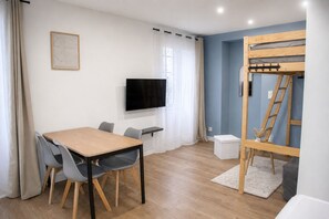 Una habitación con una mesa de madera, sillas, un televisor, una cama nido y un pequeño armario blanco.