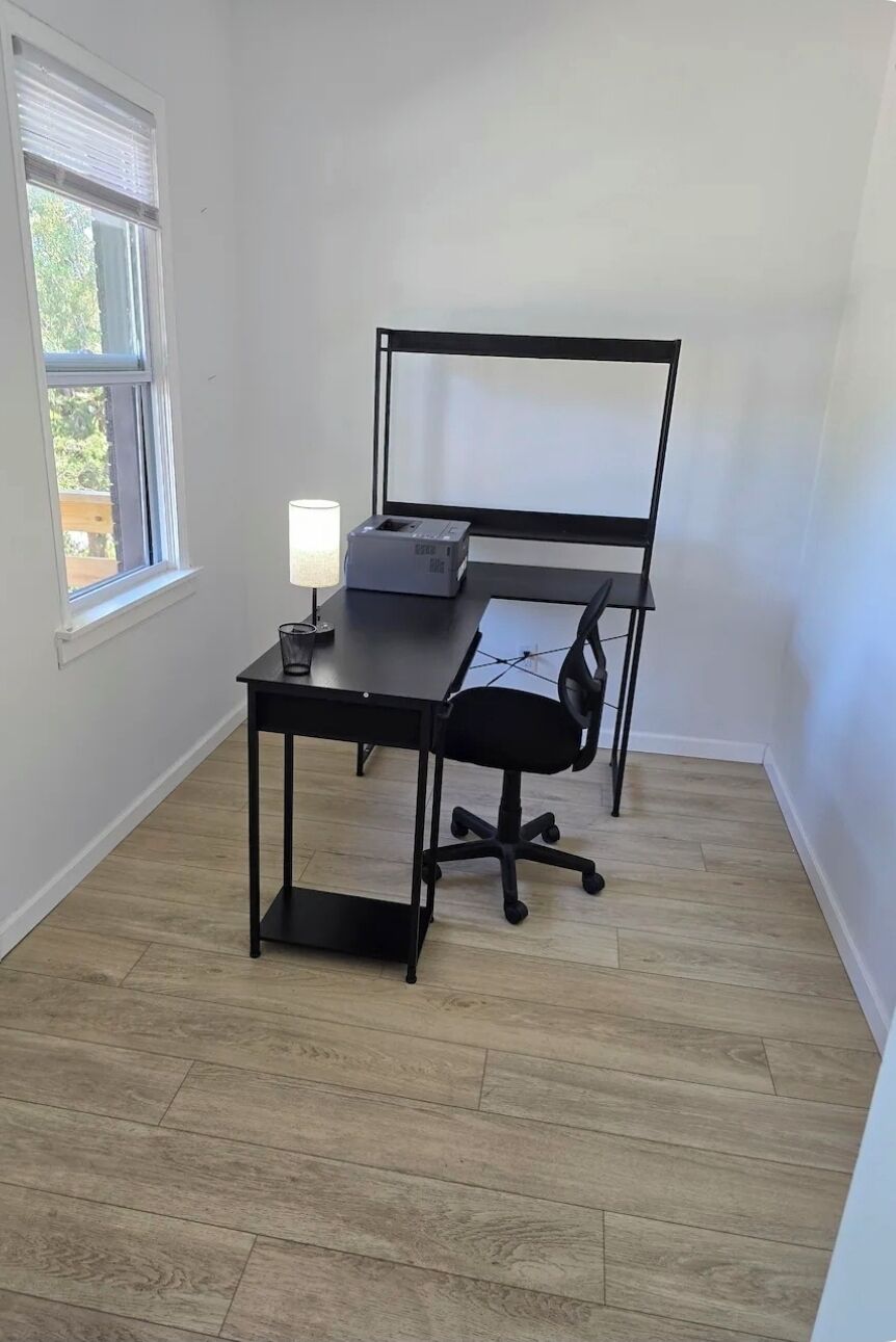 Een kamer met een bureau, stoel, lamp en raam.