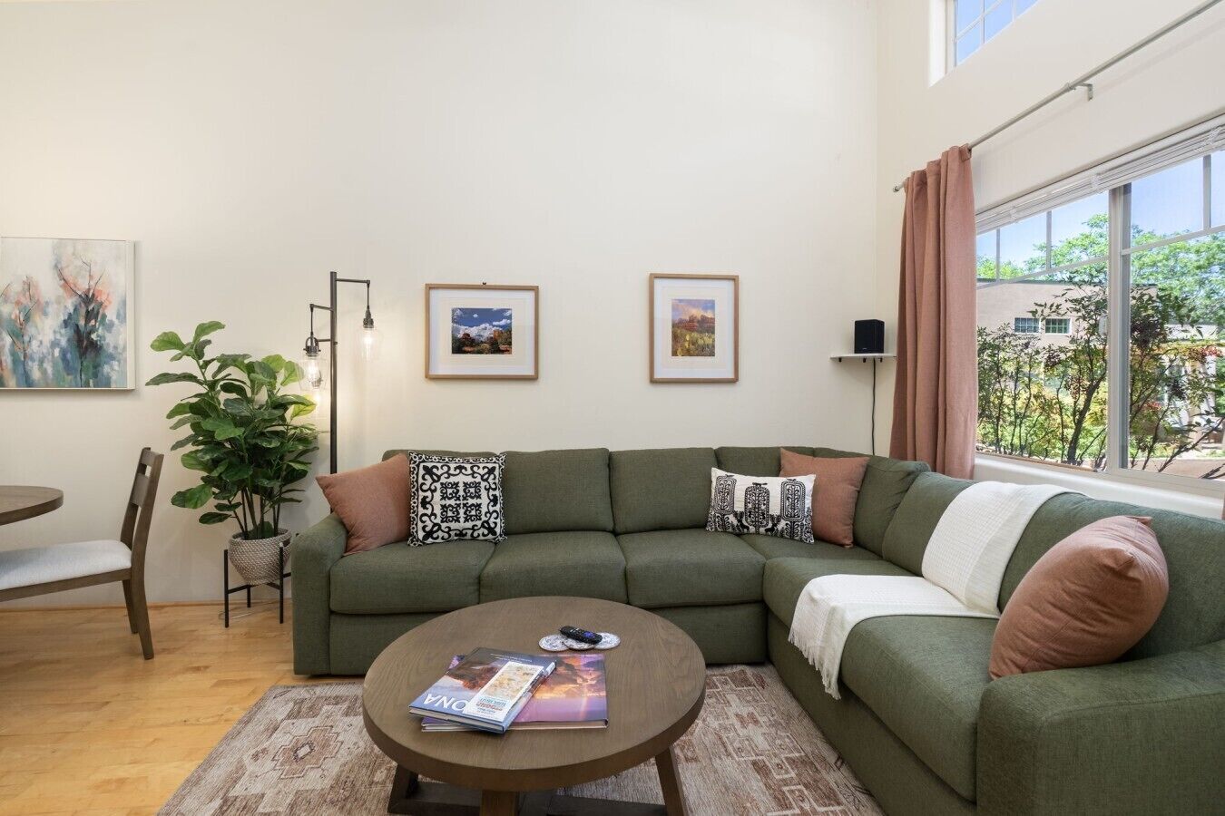 A green sofa with patterned cushions, a round coffee table with magazines, and a potted plant.