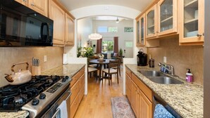 A kitchen with wooden cabinets, a granite countertop, a stove, and a dining area with a table and chairs. - Uptown Sedona Red Rock Charm | Private Patio & Nice Views (Sedona)
