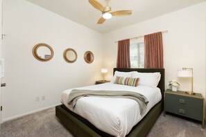Een slaapkamer met een bed, een nachtkastje, een lamp, een plafondventilator en drie spiegels aan de muur.