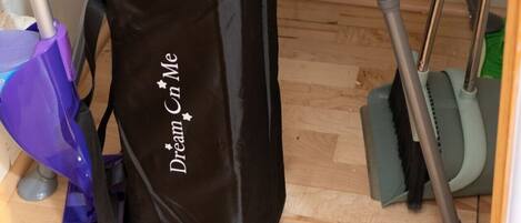 A room with a grey mobility aid, a black bag with 'Dream in Me' text, and a purple cleaning tool.
