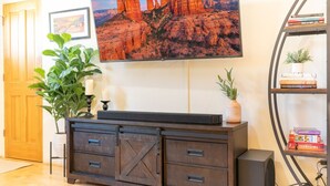 A living room with a TV, a bookshelf, a plant, and a fireplace. - Uptown Sedona Red Rock Charm | Private Patio & Nice Views (Sedona)
