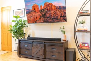 A living room with a TV, a bookshelf, a plant, and a fireplace. - Uptown Bougie Escape | Private Patio & Nice Views (Sedona)