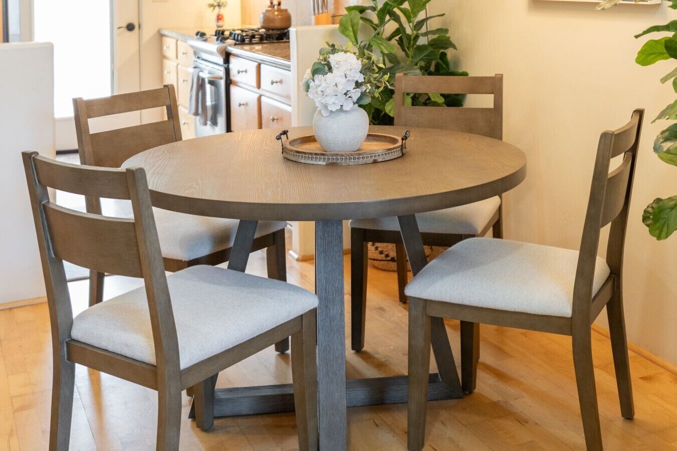 A round dining table with four chairs, a vase with flowers, and a tray on the table.