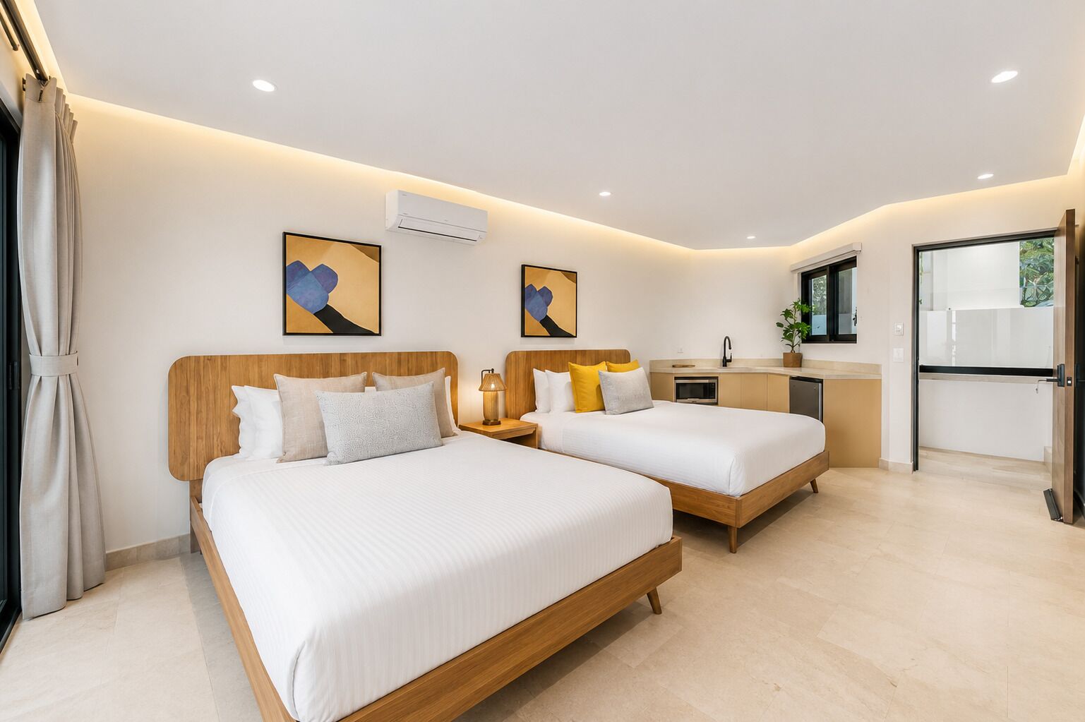 Ein Hotelzimmer mit zwei Betten, einer Küchenzeile und Bildern an den Wänden.