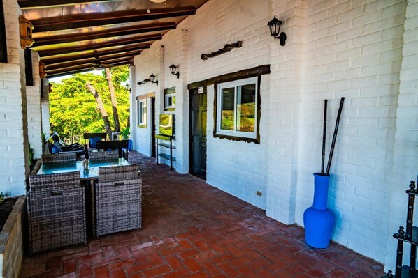 A covered patio with wicker furniture, a blue vase, and a brick floor.