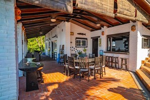 Un patio cubierto con suelo de ladrillo, mesas y sillas de madera, y una pared de ladrillo blanco con detalles decorativos.