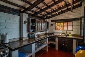 Una cocina rústica con paredes de ladrillo visto, vigas de madera, encimera de granito y una ventana con vistas coloridas.