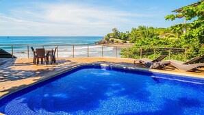 Una piscina con sillas de descanso y una mesa, con vista al océano.