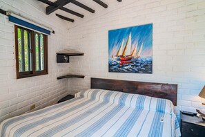 A bedroom with a bed, a painting of a sailboat, a window, and a shelf.