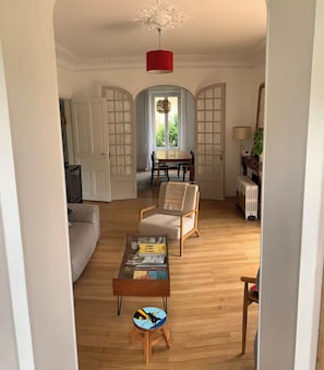 Ein Wohnzimmer mit einer Couch, einem Couchtisch mit Zeitschriften, einem Sessel und einem Esstisch mit Stühlen.