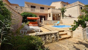 Un edificio de piedra con piscina, mobiliario exterior y una zona de estar cubierta.