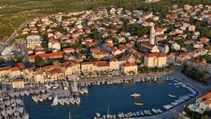 Vista aérea de un pueblo costero con un puerto deportivo, edificios históricos y una iglesia destacada.