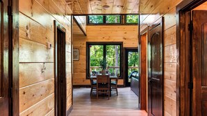 Ein Holzboden-Flur führt zu einem Essbereich mit Tisch und Stühlen, mit Blick ins Freie durch große Fenster.