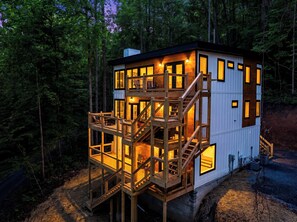A multi-level wooden cabin with a deck, surrounded by trees. - Mountain Laurel Cabin!! Heated Pool, Theatre, Hot-tub, Games, near Pigeon Forge! (Sevierville)