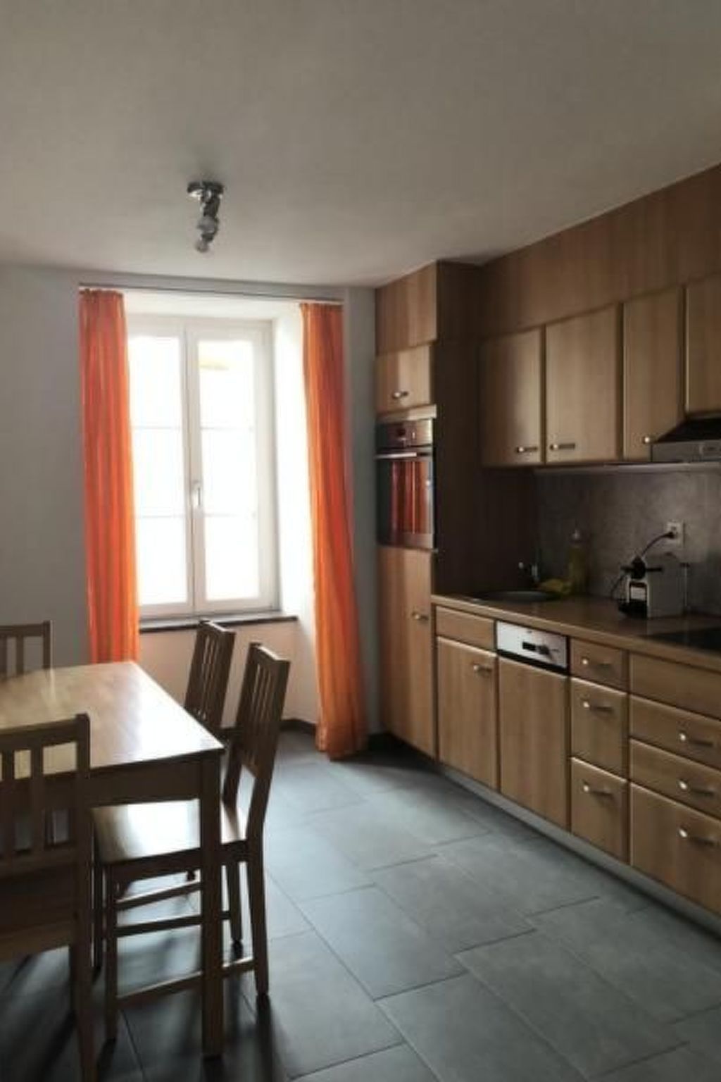 Eine Küche mit Holzschränken, einem Esstisch mit Stühlen und einem Fenster mit Vorhängen.