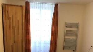 A bedroom with a wooden floor, a bed with a white mattress, a wooden wardrobe, a radiator, and a window with curtains. - Chasa Strimer, (Zernez) by Interhome (Zernez)