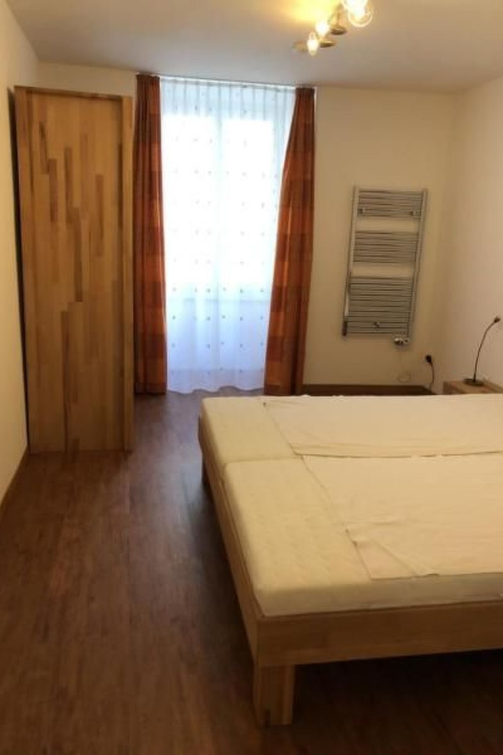 Ein Schlafzimmer mit Holzboden, einem Bett, einem Heizkörper und einer Tür.