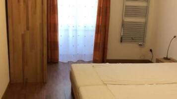 Ein Schlafzimmer mit Holzboden, einem Bett, einem Heizkörper und einer Tür.