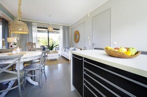 A modern kitchen with a central island, dining area with a round table and chairs, and a living area with a sofa and a coffee table. - Koupeli 3 Bedroom Apartment (Chania)