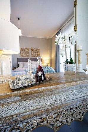 A hotel room with a bed, a bedside table with a tray of glasses, a lamp, and decorative items. - Koupeli 3 Bedroom Apartment (Chania)