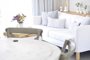 A white sofa with striped pillows, a round table with a chair, and a vase of flowers. - Koupeli 3 Bedroom Apartment (Chania)