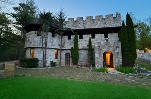 Un edificio simile a un castello, con mura in pietra, un arco centrale e un prato curato.