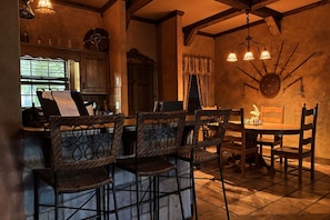 Un interior rústico con una mesa de comedor, sillas de mimbre, una zona de bar y un reloj de pared decorativo.