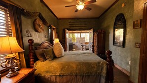 Ein Schlafzimmer mit Bett, Deckenventilator, Nachttisch mit Lampe und Blick ins Freie.